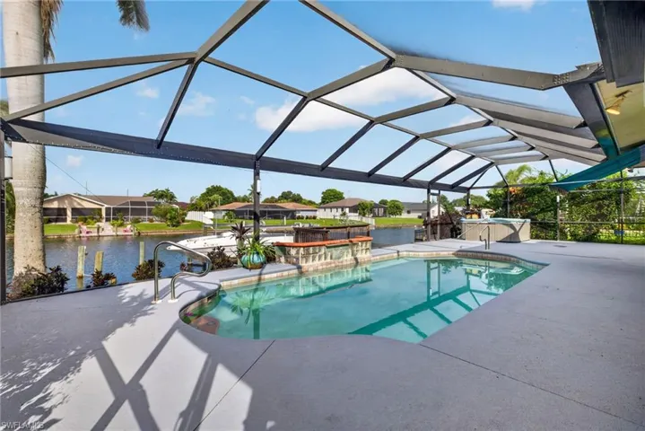 Screened outdoor living area with a built-in swimming pool, integrated spa, and canal access