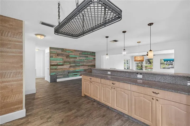 Expansive counter bar with a stone-finish surface, light wood-finish cabinetry, and pendant lighting