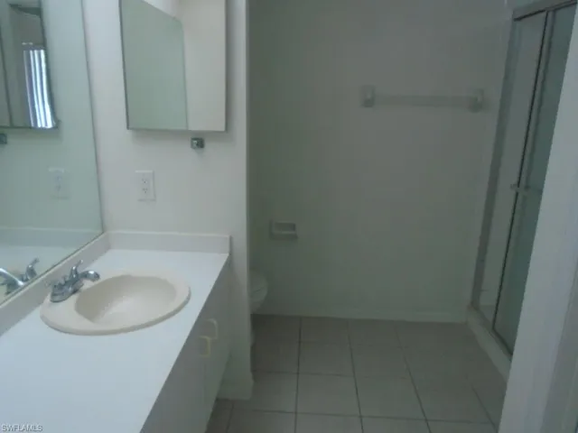 Bathroom featuring tile floors, a shower with door, large vanity, and toilet