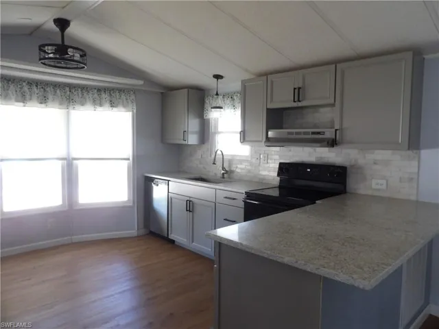 Kitchen featuring a peninsula, black range with electric cooktop, decorative backsplash, pendant lighting, and laminated flooring