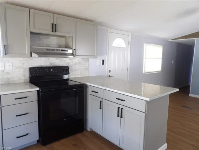 Open Kitchen with black / electric stove, a peninsula, laminated finished floors, tasteful backsplash, and light stone counters