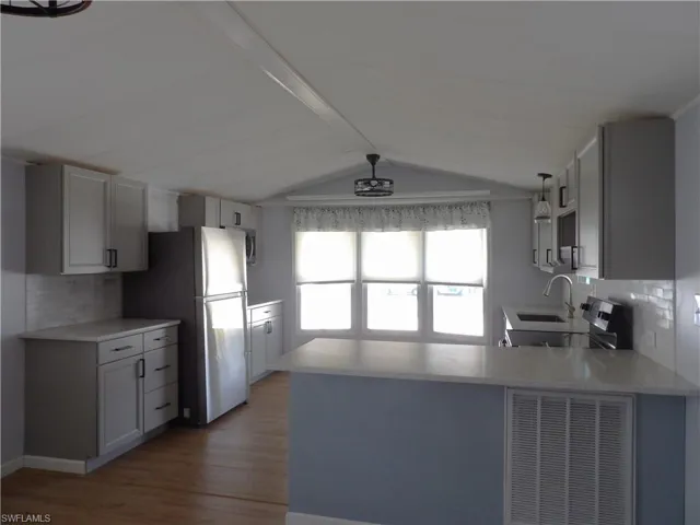 Kitchen featuring decorative backsplash, a peninsula, stainless steel appliances, gray cabinetry, and dark wood finished floors