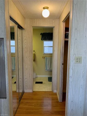 Hallway with electric panel, a textured ceiling, baseboards, and wood finished floors