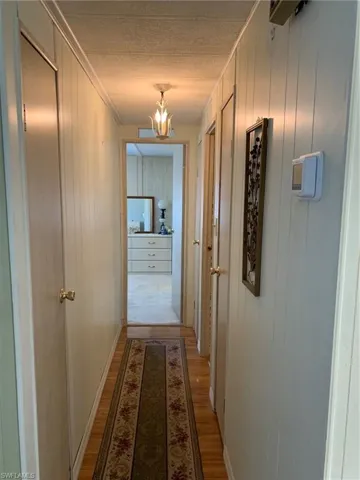 Hallway featuring a chandelier, light wood-style flooring, a textured ceiling, and ornamental molding