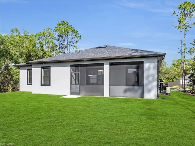 Rear view of house featuring a yard, roof with shingles, a sunroom, and stucco siding