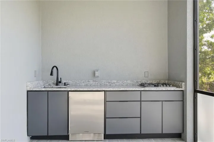 Bar with gray cabinetry, stainless steel appliances, light stone counters, and a textured wall