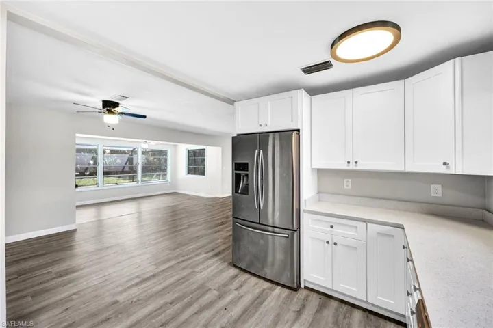 Kitchen with ceiling fan, light wood-type flooring, stainless steel refrigerator with ice dispenser, and white cabinetry