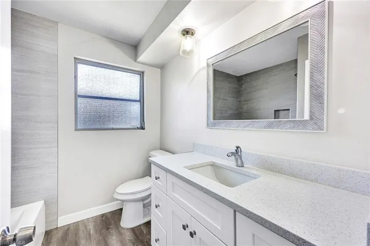 Full bathroom with hardwood / wood-style flooring, vanity, tiled shower / bath, and toilet