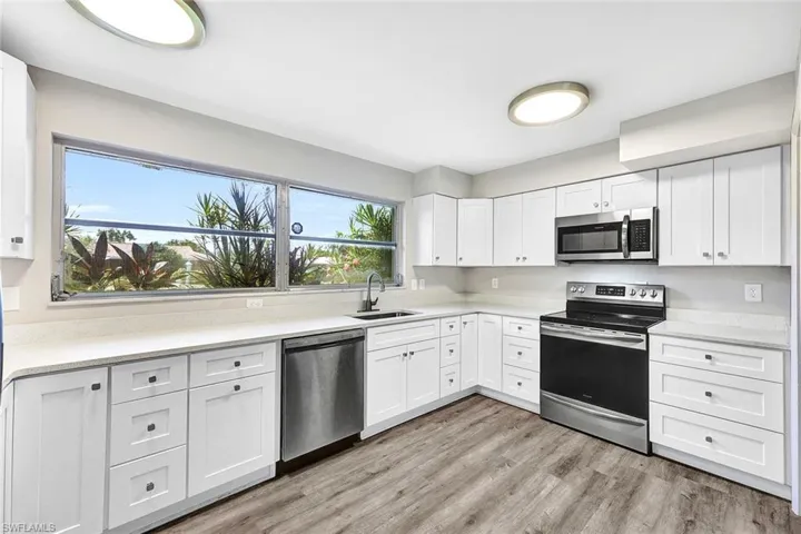 Kitchen with appliances with stainless steel finishes, sink, light hardwood / wood-style flooring, and white cabinets