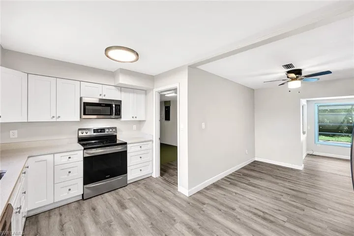 Kitchen with appliances with stainless steel finishes, white cabinets, ceiling fan, and light hardwood / wood-style floors