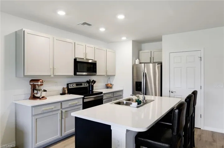 Kitchen with sink, a breakfast bar area, gray cabinetry, a kitchen island with sink, and stainless steel appliances