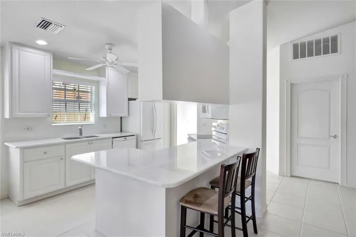 Kitchen with white appliances, a breakfast bar, a sink, and visible vents