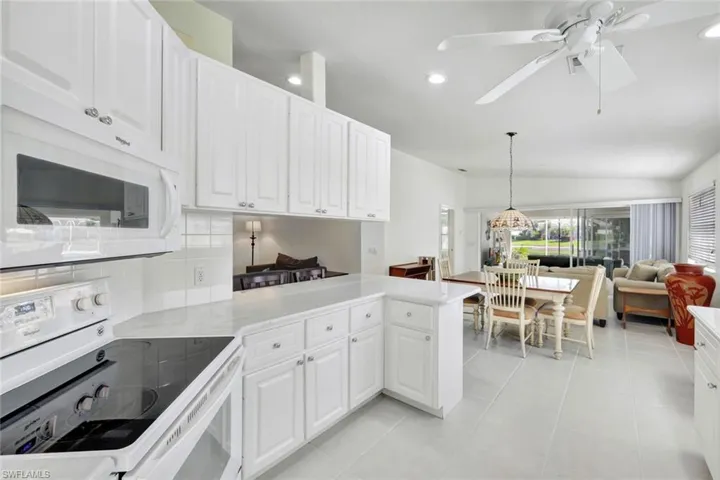 Kitchen with a peninsula, white appliances, white cabinets, and tasteful backsplash