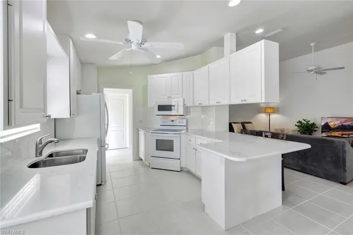 Kitchen featuring decorative backsplash, white cabinetry, a sink, white appliances, and a peninsula