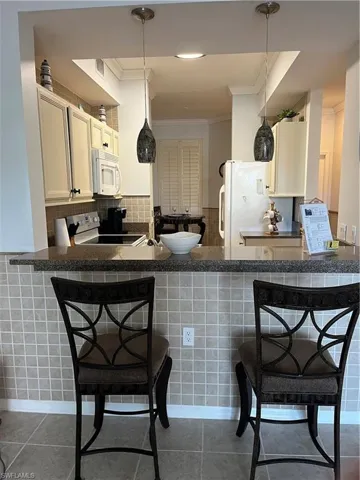 Kitchen featuring a breakfast bar area, ornamental molding, decorative light fixtures, fridge, and range
