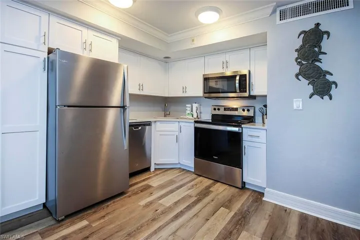Kitchen featuring stainless steel appliances, white cabinets, sink, light, LVP floors, and crown molding