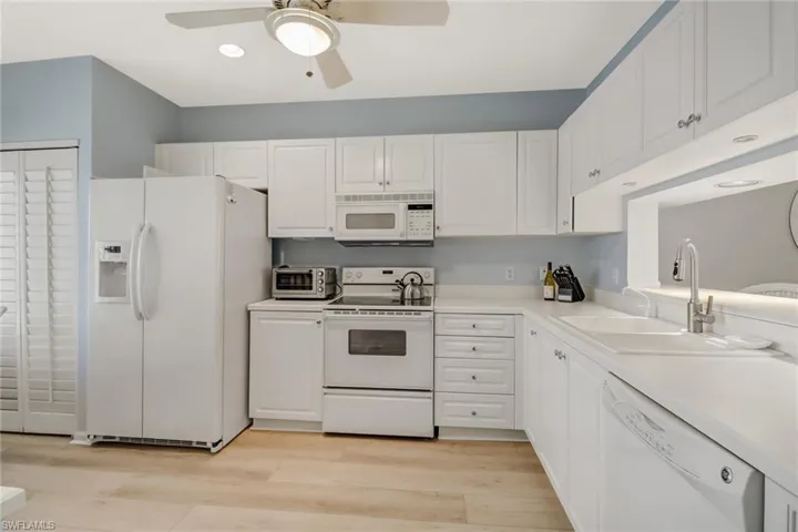 Kitchen with white appliances, light countertops, white cabinets, and light wood-style flooring