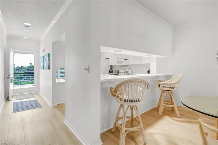 Kitchen with a breakfast bar, light wood-style floors, light countertops, ornamental molding, and a peninsula