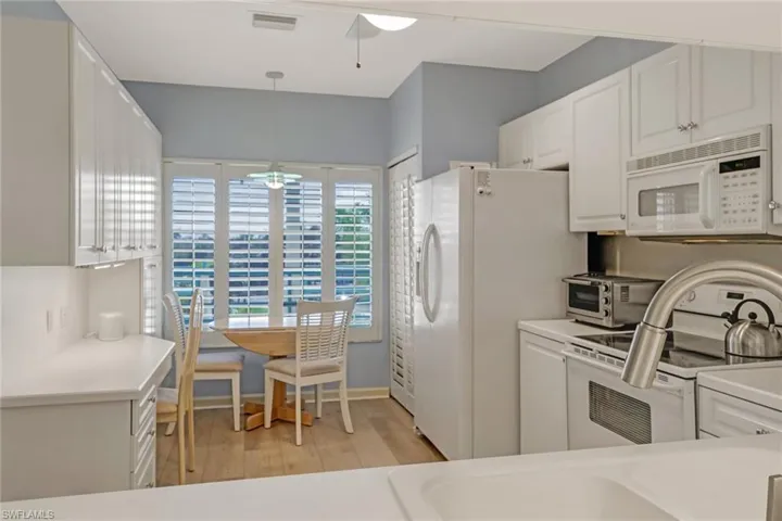 Kitchen featuring white appliances, white cabinetry, light countertops, light wood finished floors, and hanging light fixtures