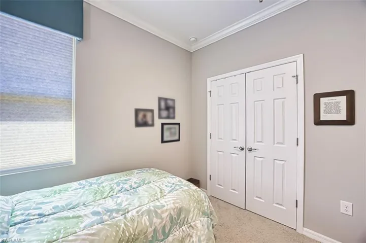 Bedroom with a closet, light carpet, baseboards, and ornamental molding