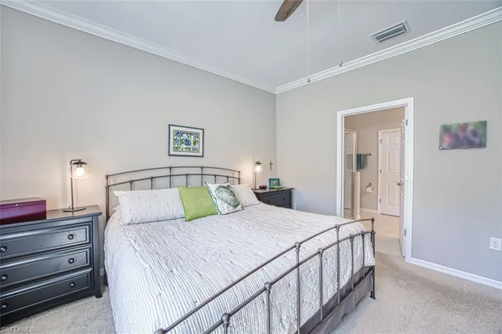 Bedroom featuring visible vents, ornamental molding, ensuite bath, carpet floors, and baseboards