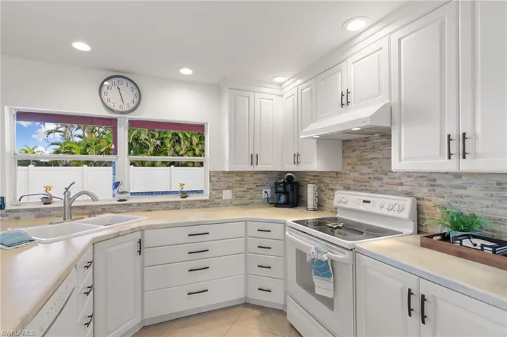 Kitchen featuring white appliances, white cabinetry, light countertops, decorative backsplash, and recessed lighting