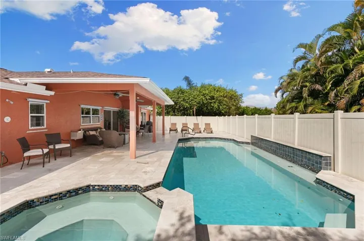 Pool with Travertine pool deck, covered lounge area, a fenced backyard, outdoor shower, drinking fountain and a hot tub