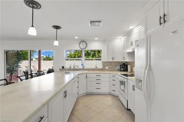 Kitchen featuring white appliances, white cabinets, backsplash, hanging light fixtures, and recessed lighting
