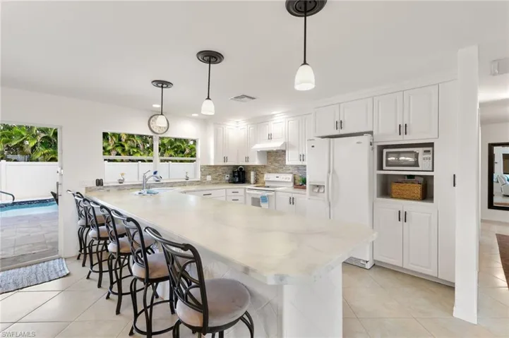 Kitchen with white cabinetry, white appliances, decorative light fixtures, and a kitchen bar