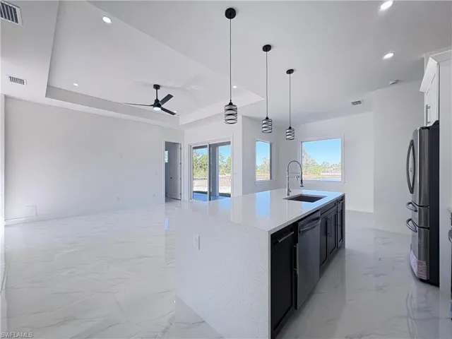 Kitchen with a raised ceiling, sink, an island with sink, and appliances with stainless steel finishes