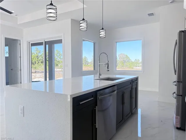 Kitchen with hanging light fixtures, sink, light stone countertops, an island with sink, and appliances with stainless steel finishes