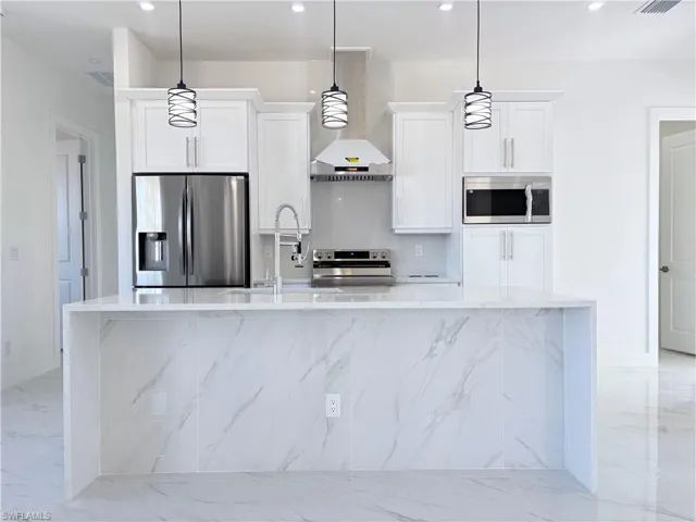 Kitchen with white cabinetry, pendant lighting, stainless steel appliances, and light stone counters