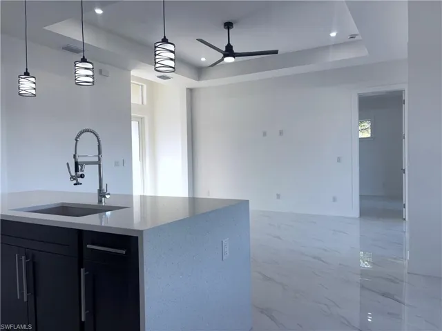 Kitchen with a center island with sink, decorative light fixtures, a raised ceiling, and sink