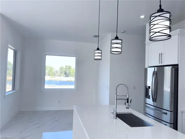 Kitchen featuring stainless steel fridge, sink, light stone countertops, and decorative light fixtures