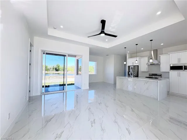 Kitchen with a tray ceiling, white cabinets, stainless steel appliances, and wall chimney range hood