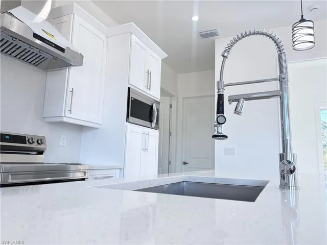 Kitchen featuring stainless steel appliances, light stone counters, white cabinetry, and range hood