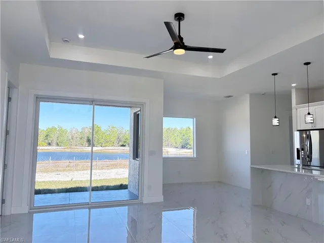 Unfurnished living room featuring ceiling fan, a water view, and a tray ceiling