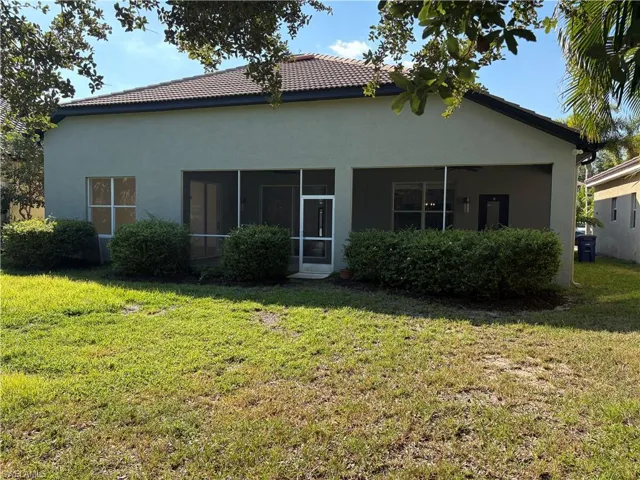 Rear view of house featuring stucco siding, a lawn, a sunroom, and a tile roof