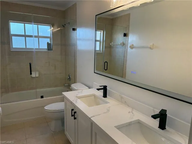 Bathroom with double vanity, plenty of natural light, shower / bath combination with glass door, and light tile patterned floors