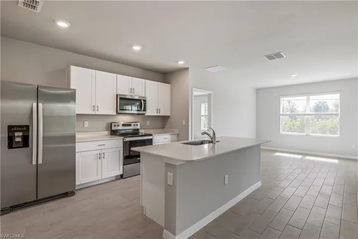 Kitchen featuring appliances with stainless steel finishes, white cabinetry, sink, and an island with sink