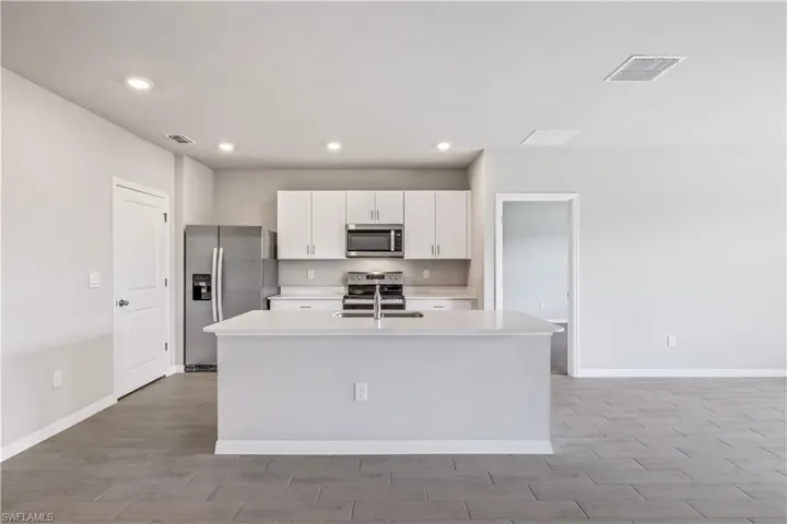 Kitchen with white cabinetry, stainless steel appliances, sink, and a center island with sink