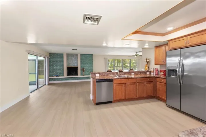 Open-concept interior featuring wood-finish flooring, a kitchen with wood cabinetry and stone countertops, stainless steel appliances, and a fireplace with tile surround