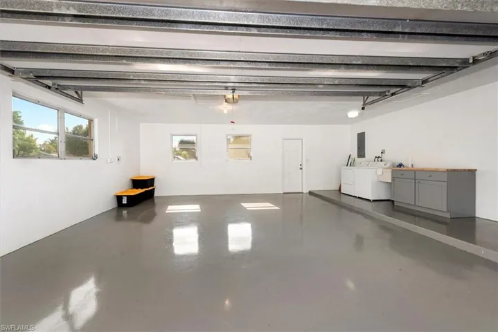 Spacious garage featuring a durable gray epoxy floor, multiple windows for natural light, a utility sink, and built-in cabinetry with a wood-finish countertop