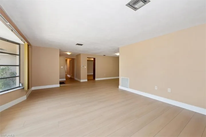 Spacious room featuring light wood-finish flooring, neutral wall tones, white baseboards, and a large multi-pane window