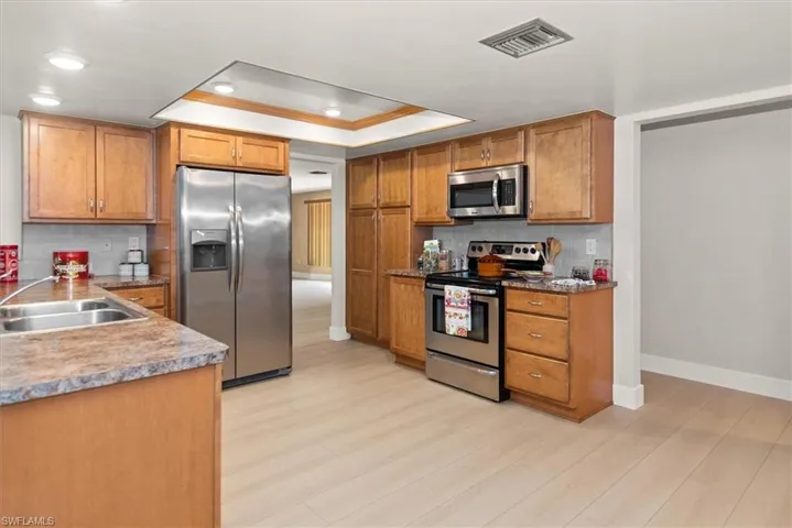 Kitchen featuring light wood-finish flooring, wood cabinetry, and stainless steel appliances including a double-door refrigerator, electric range, and built-in microwave