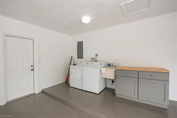 Utility space featuring an epoxy coated floor, built-in cabinetry with a wood-finish countertop, and a utility sink