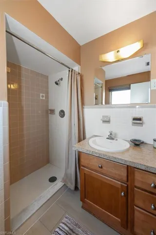 Bathroom featuring a tiled walk-in shower, a wood-finish vanity with a built-in sink, a light-toned countertop, and an illuminated mirror