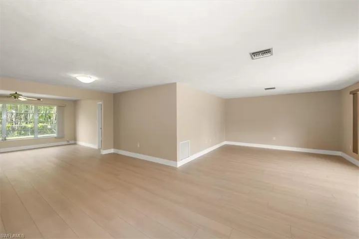 Expansive room with light wood-finish flooring, neutral wall tones, and white baseboards