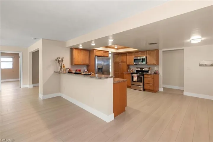 Open-concept kitchen featuring light wood cabinetry, stainless steel appliances, granite countertops, and a breakfast bar