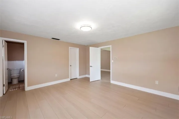 Spacious room featuring light wood-finish flooring, neutral wall paint, and white baseboards